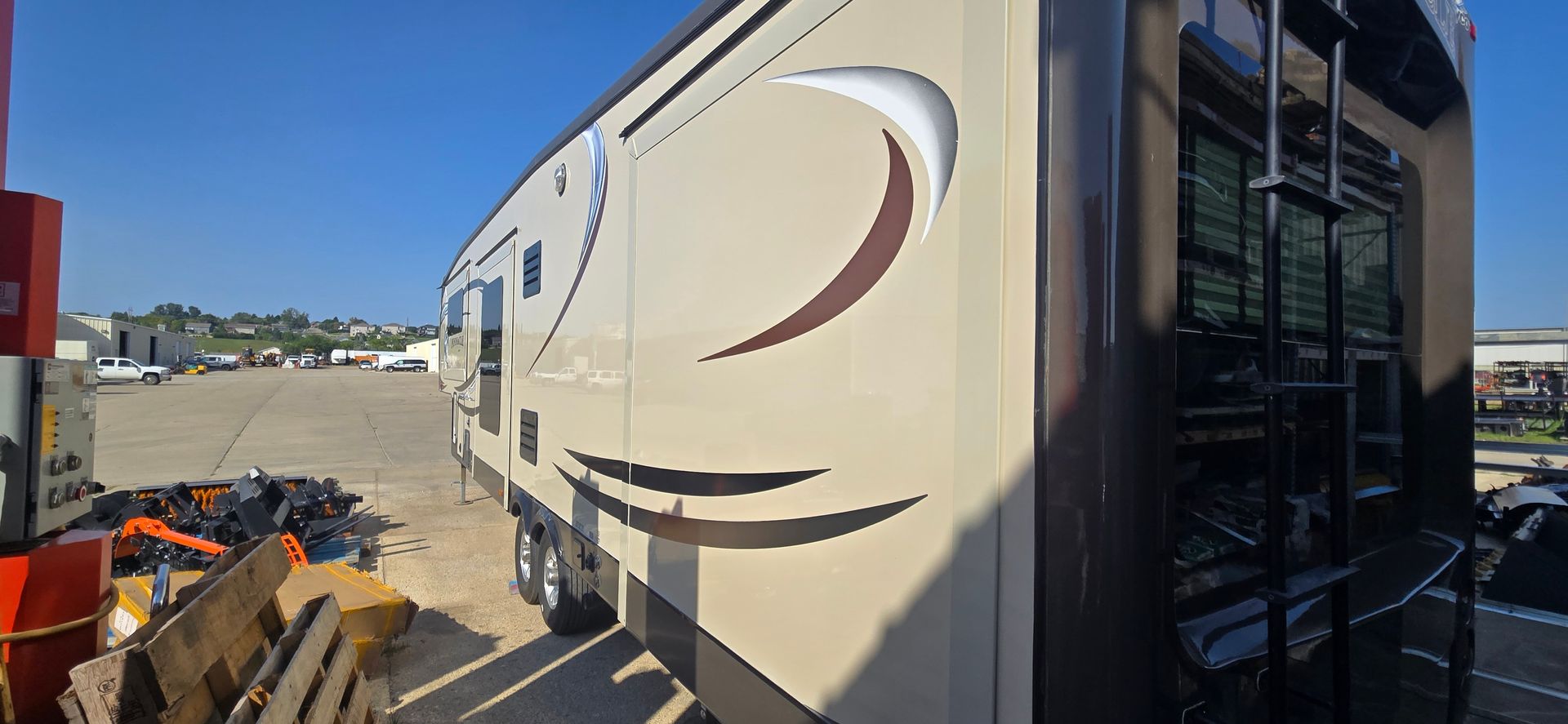 Beige RV parked beside a lot, with a curved stripe and a black entry door.