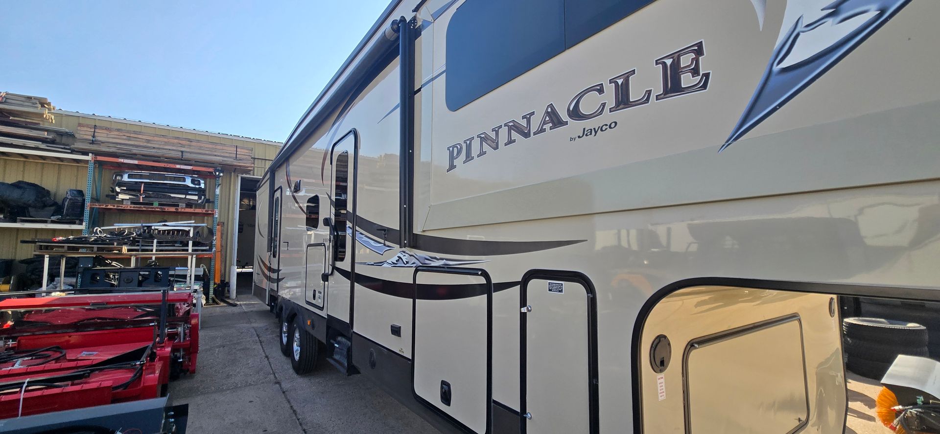 White Pinnacle RV parked beside red utility vehicles in a lot