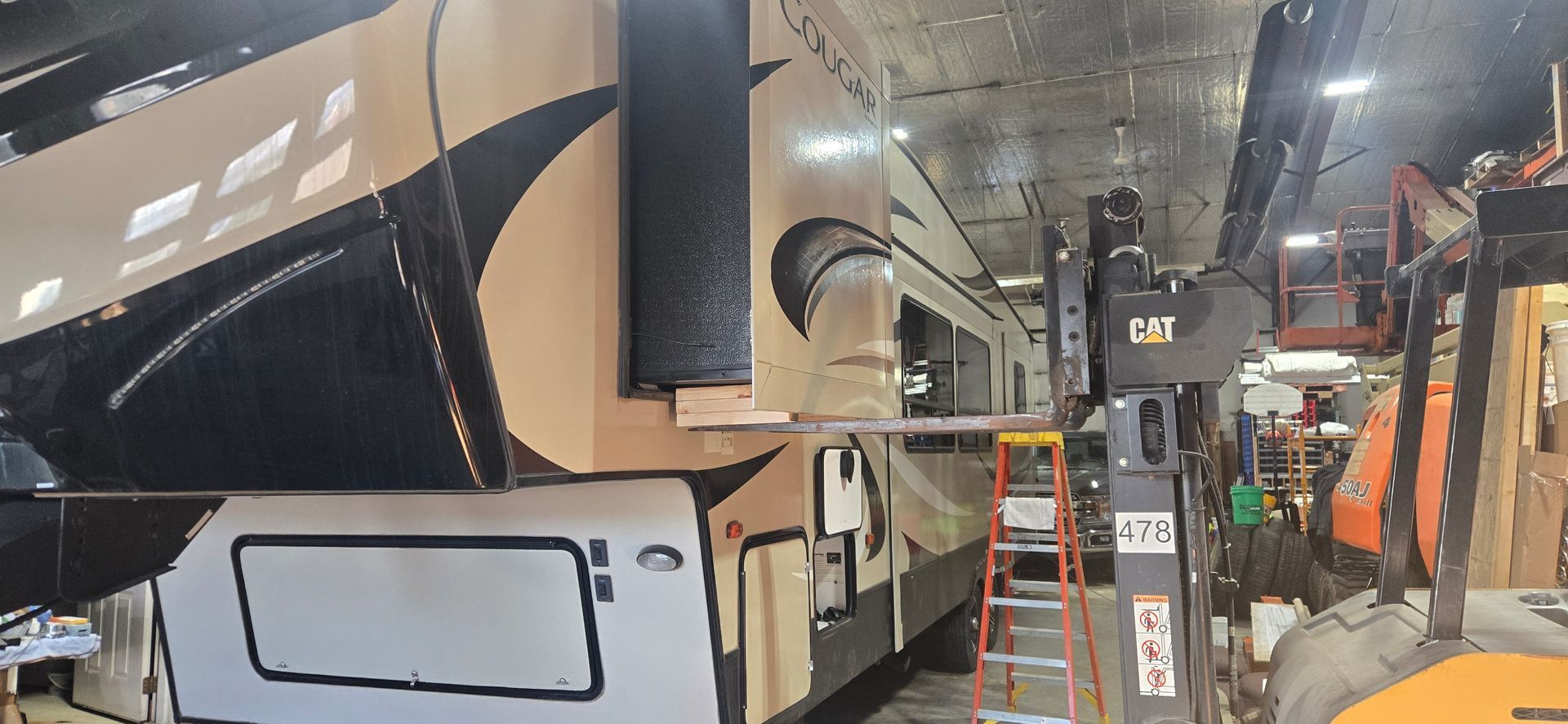 Interior of a bus depot with a white and black coach, orange ladders, and overhead fixtures