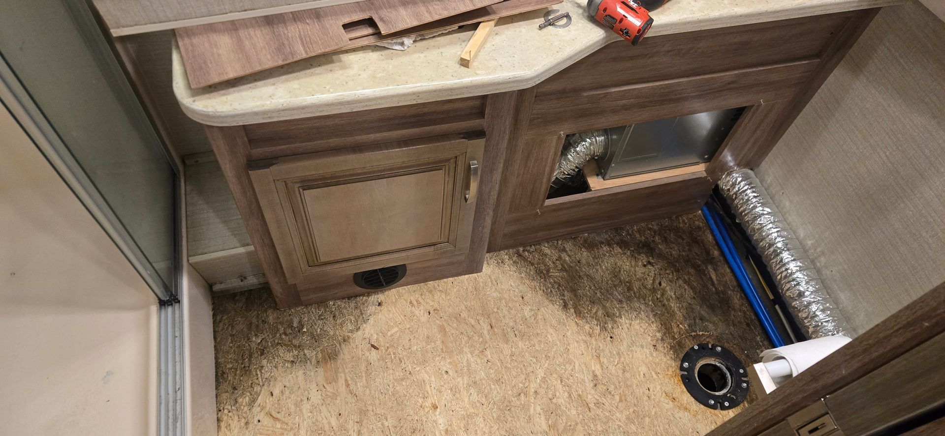 Small bathroom sink cabinet with open storage, beige carpet, and a blue toilet paper holder on the floor.