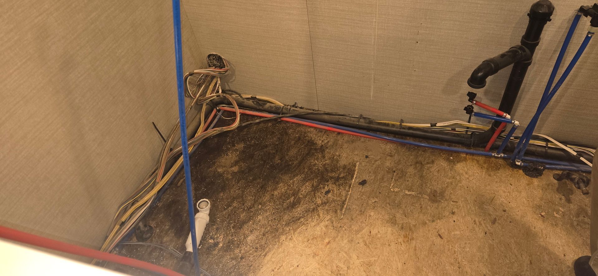 Damaged corner of a carpeted room with exposed wires and blue poles against the walls
