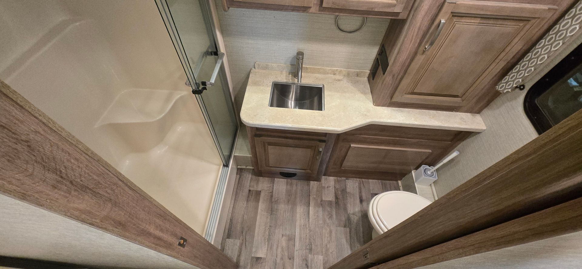 Compact RV bathroom with wood cabinets, sink, toilet, and shower stall