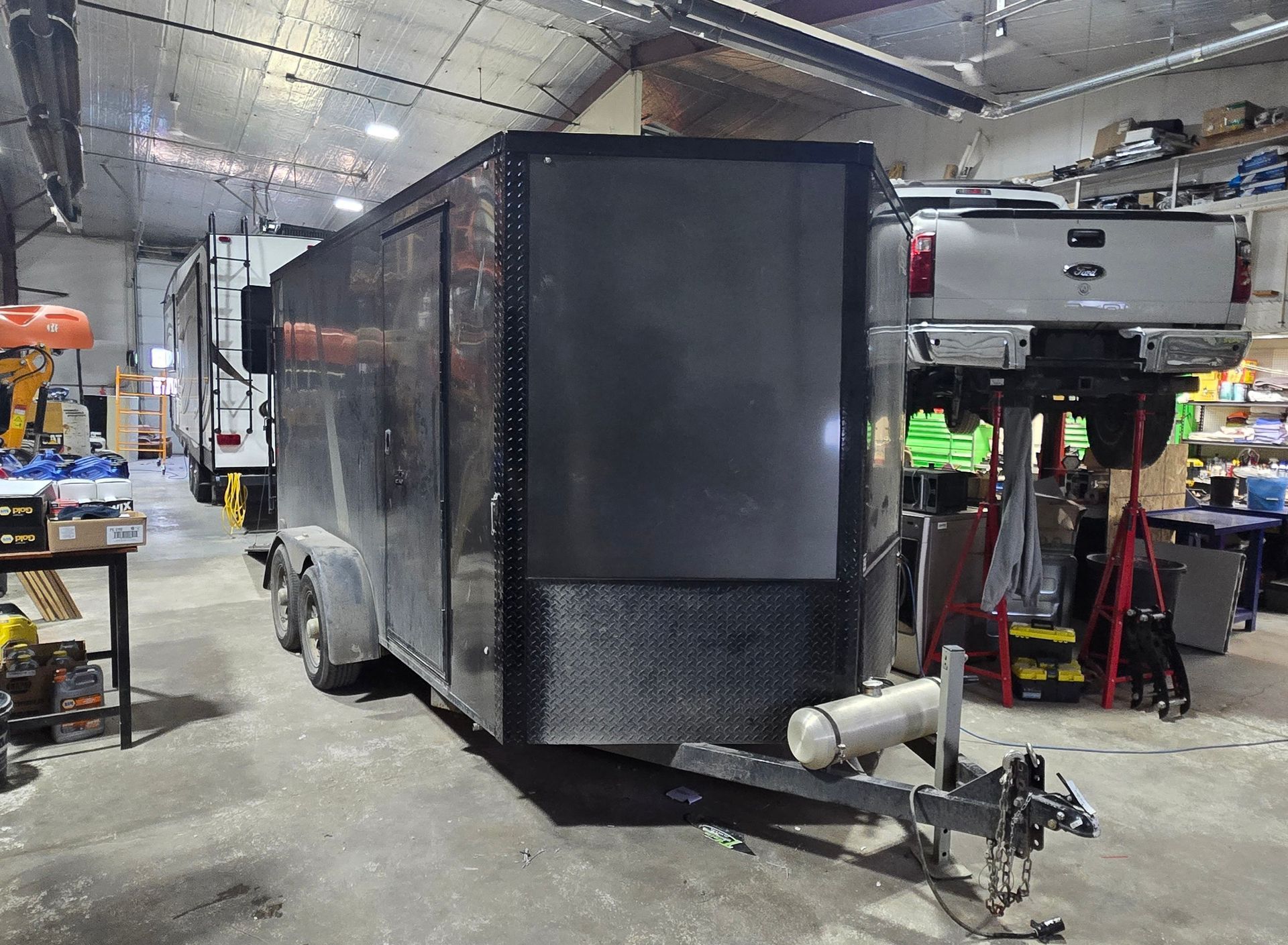 Black enclosed trailer in a workshop, with a white trailer nose and tools around it.