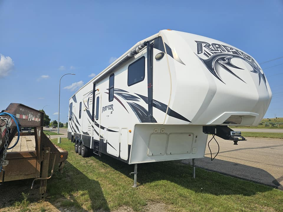 White and gray RV trailer parked on grass by a road under a blue sky