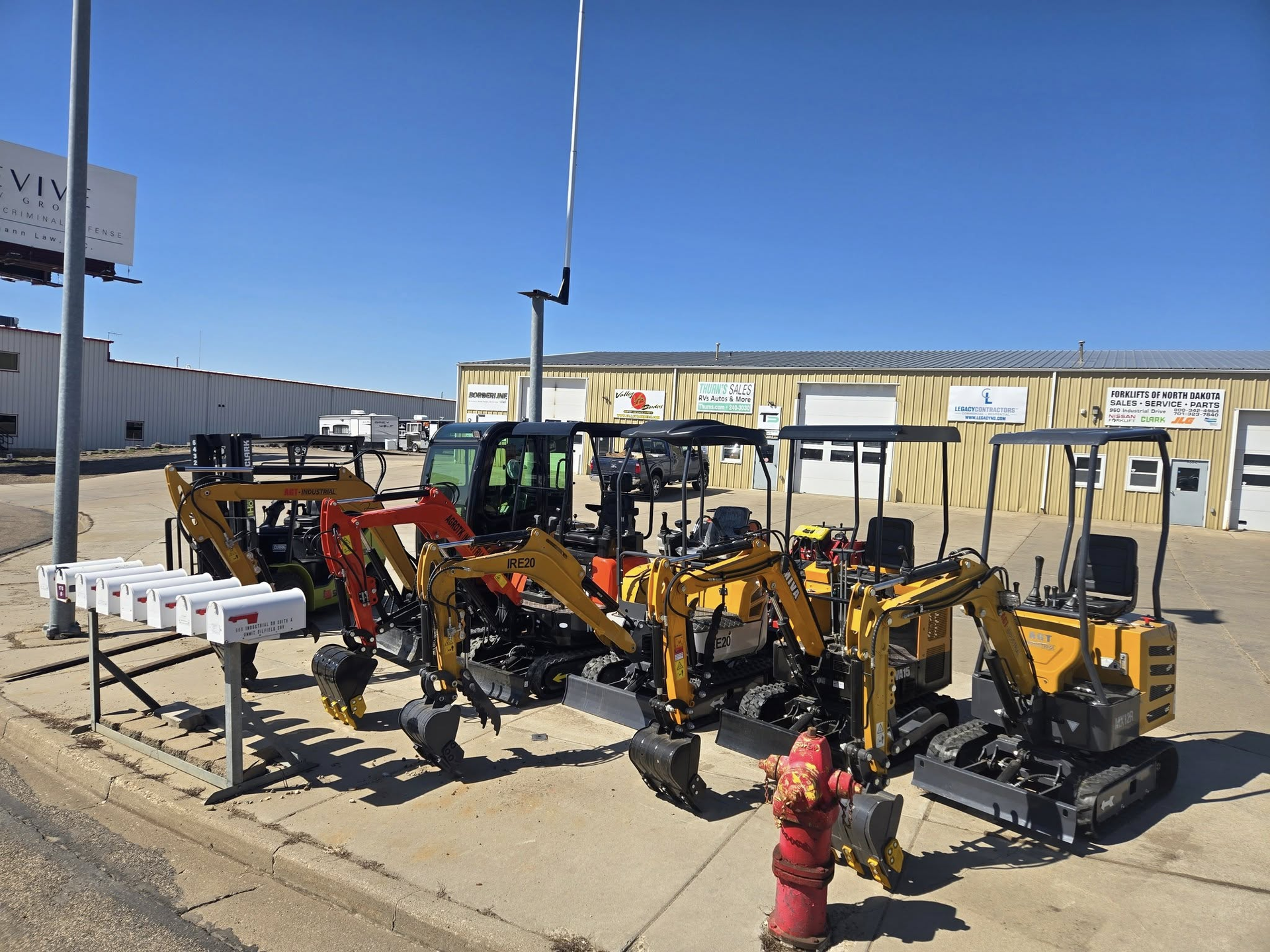 Yellow backhoe loaders parked beside a red fire hydrant under a clear blue sky.