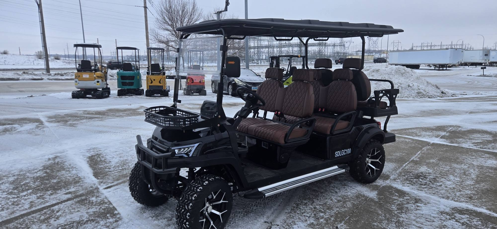 Black utility golf cart with roof parked on a snowy lot, with other carts in the background