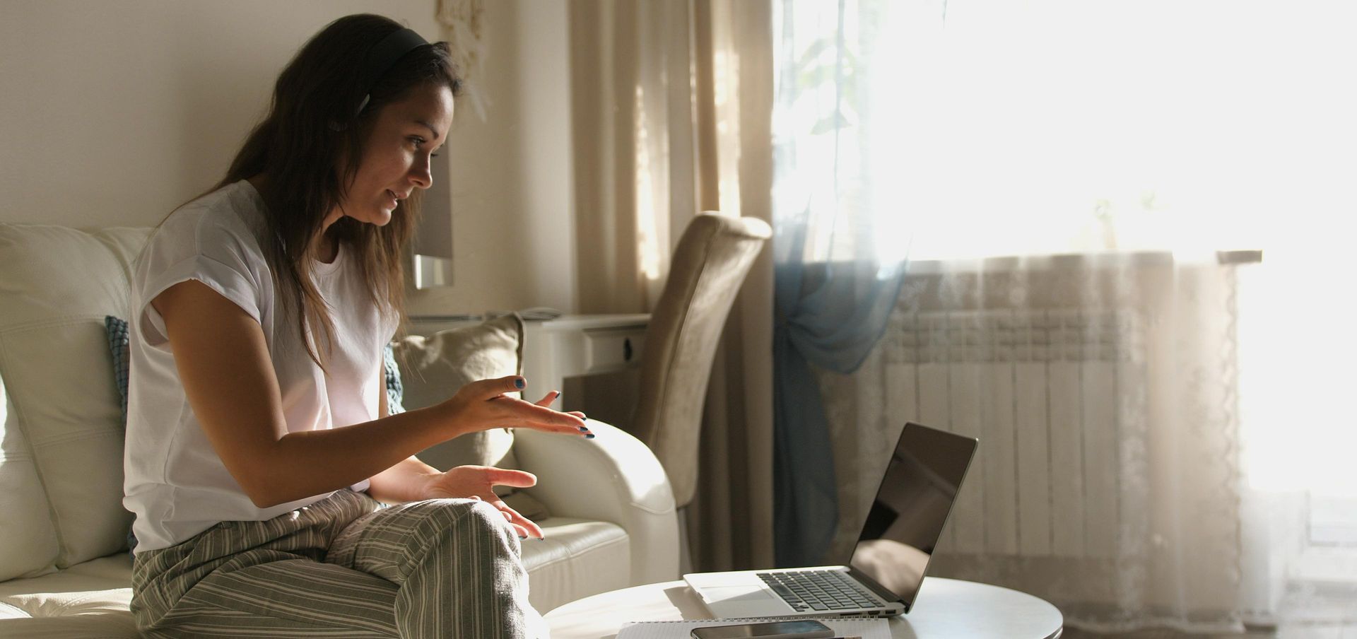 Woman on video call, seated in a living room, gesturing with hands.