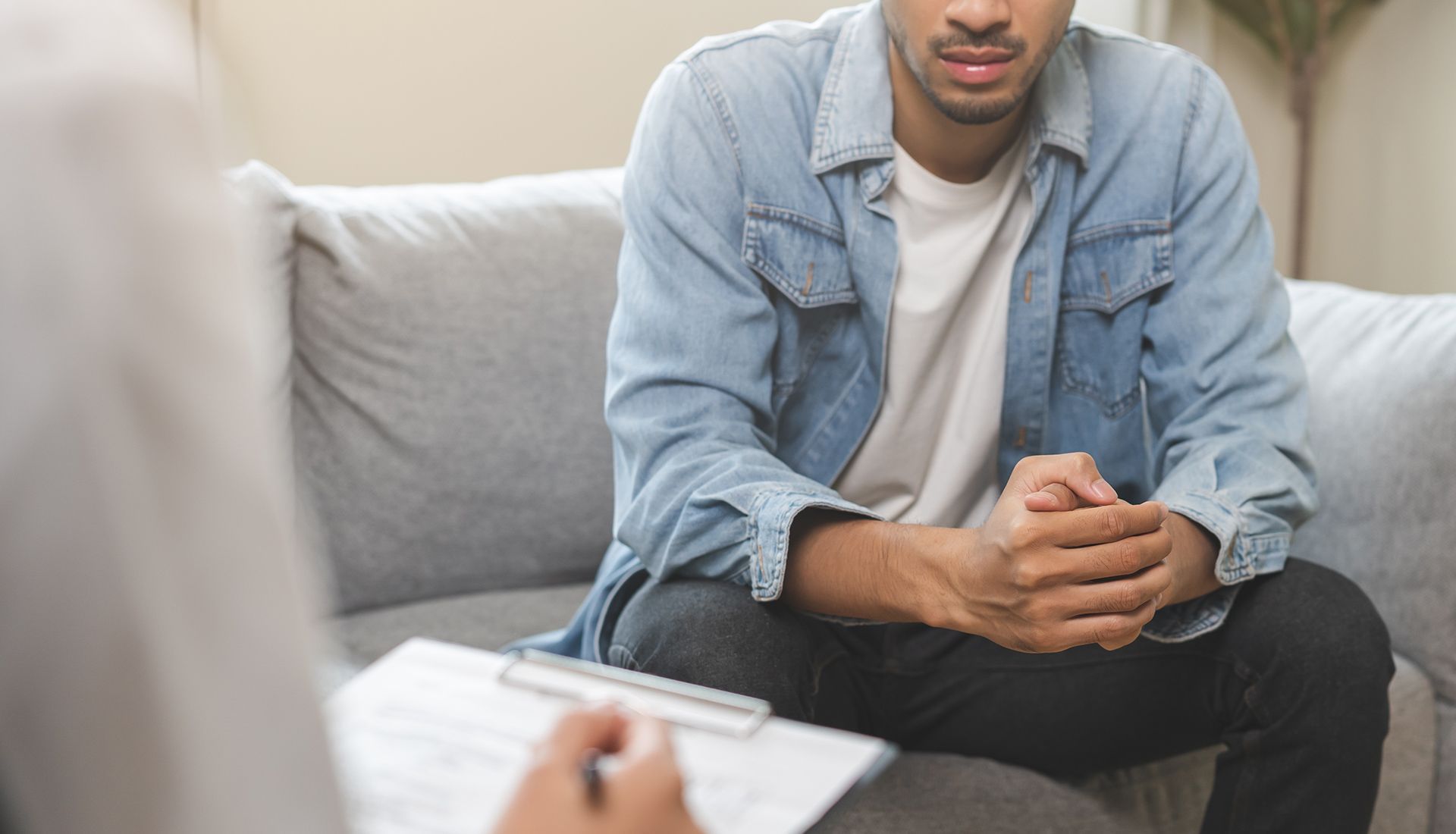 Man in therapy, sitting on a couch, talking to therapist with notes.