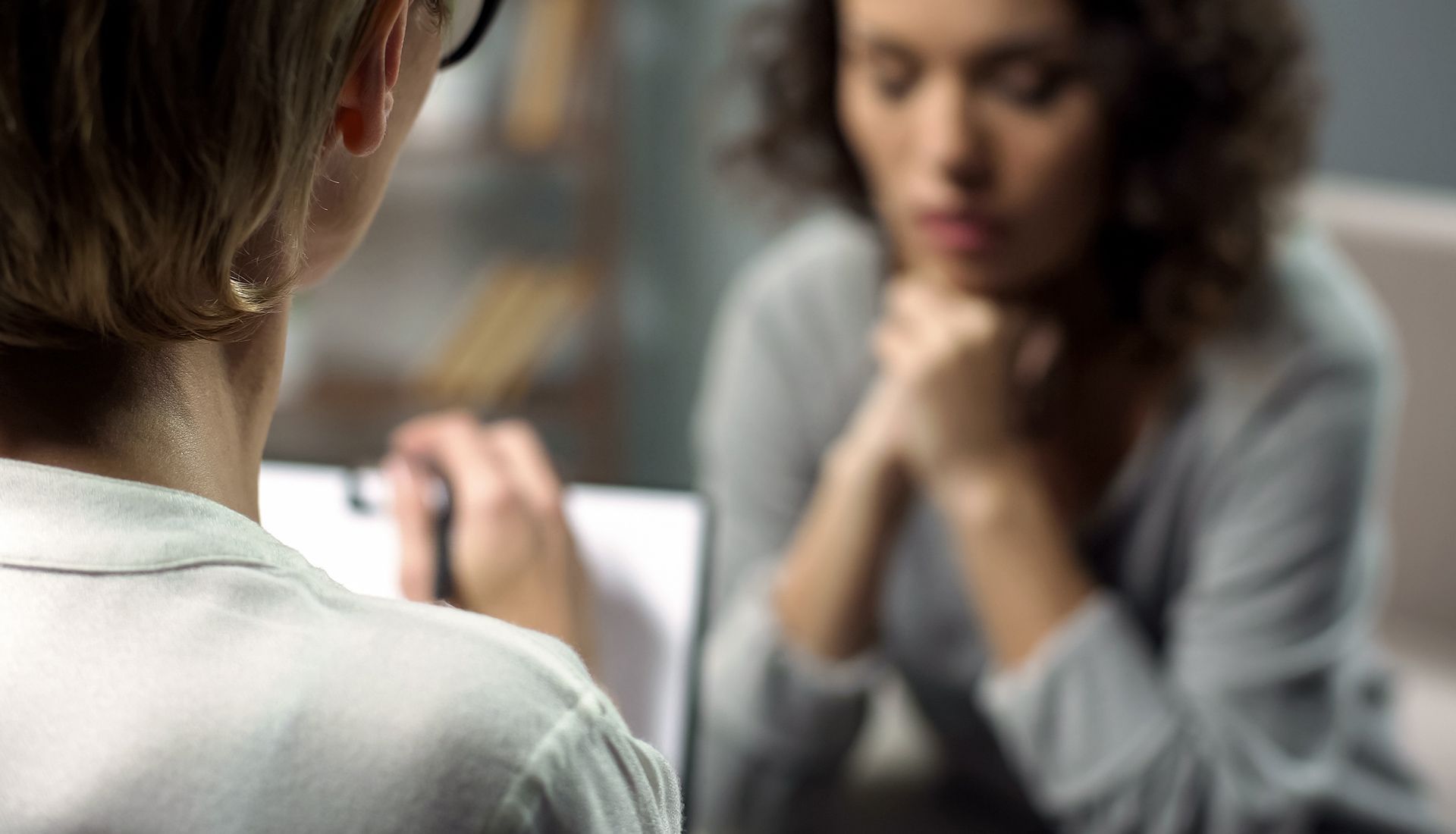Woman in therapy session; therapist taking notes.