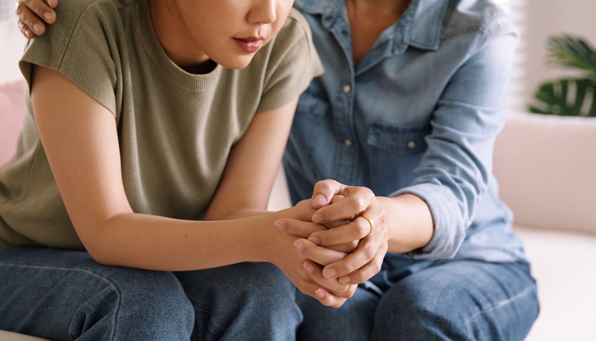 Woman in distress comforted by another, hand held and shoulder touched.