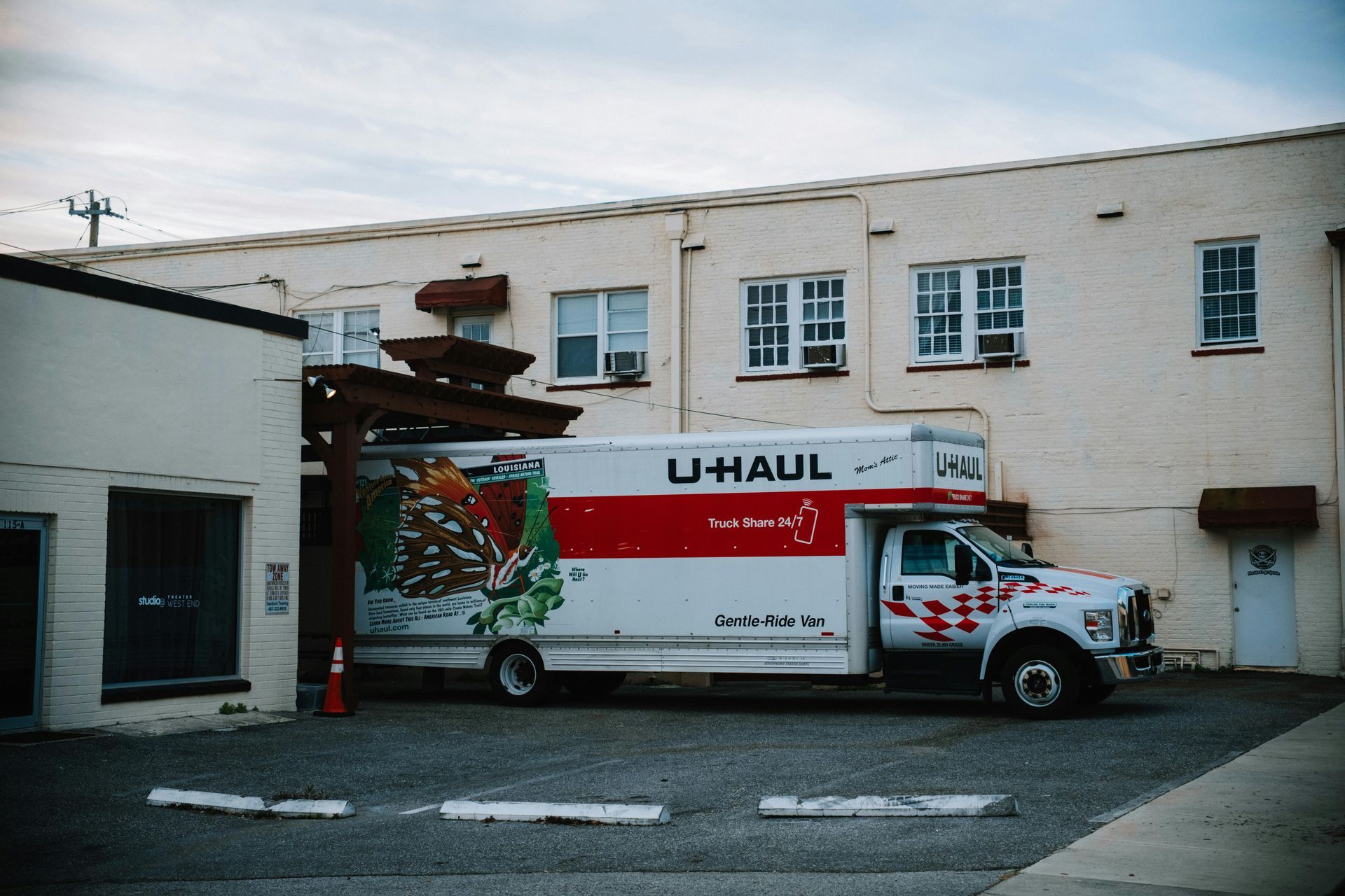 U-Haul truck parked near a light yellow building. Red and white branding. Cloudy sky.