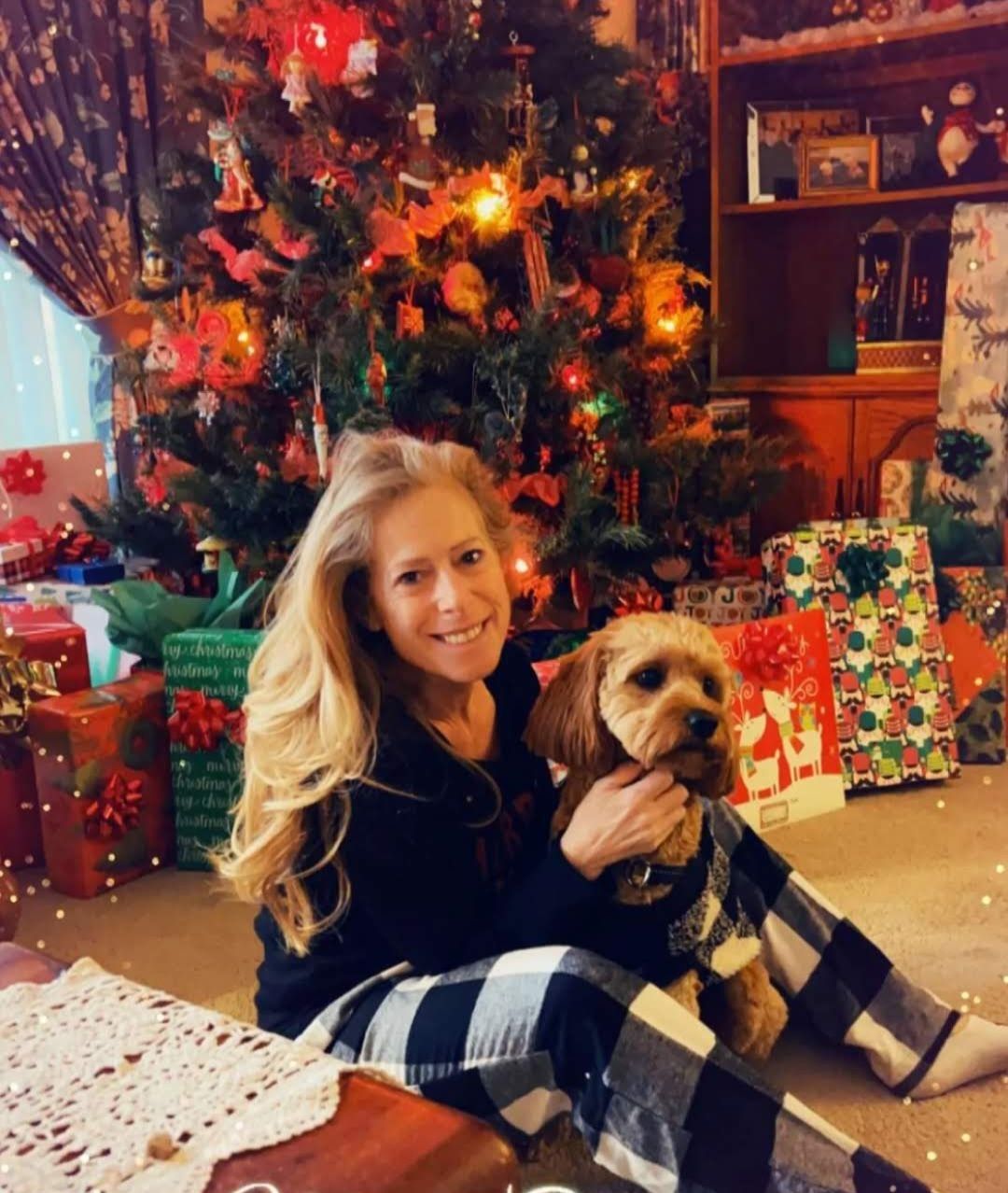 A person with a beard and hair pulled back stands in a gym, wearing a light blue t-shirt with arms crossed, looking ahead.
