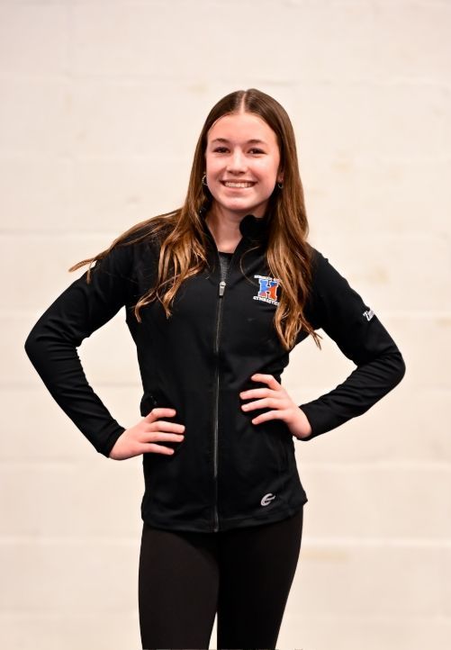 A smiling person sits in a blue armchair in front of a brick fireplace decorated with Christmas lights and a tree.