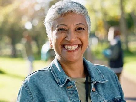 A woman is making a heart shape with her hands in front of the sun at sunset.
