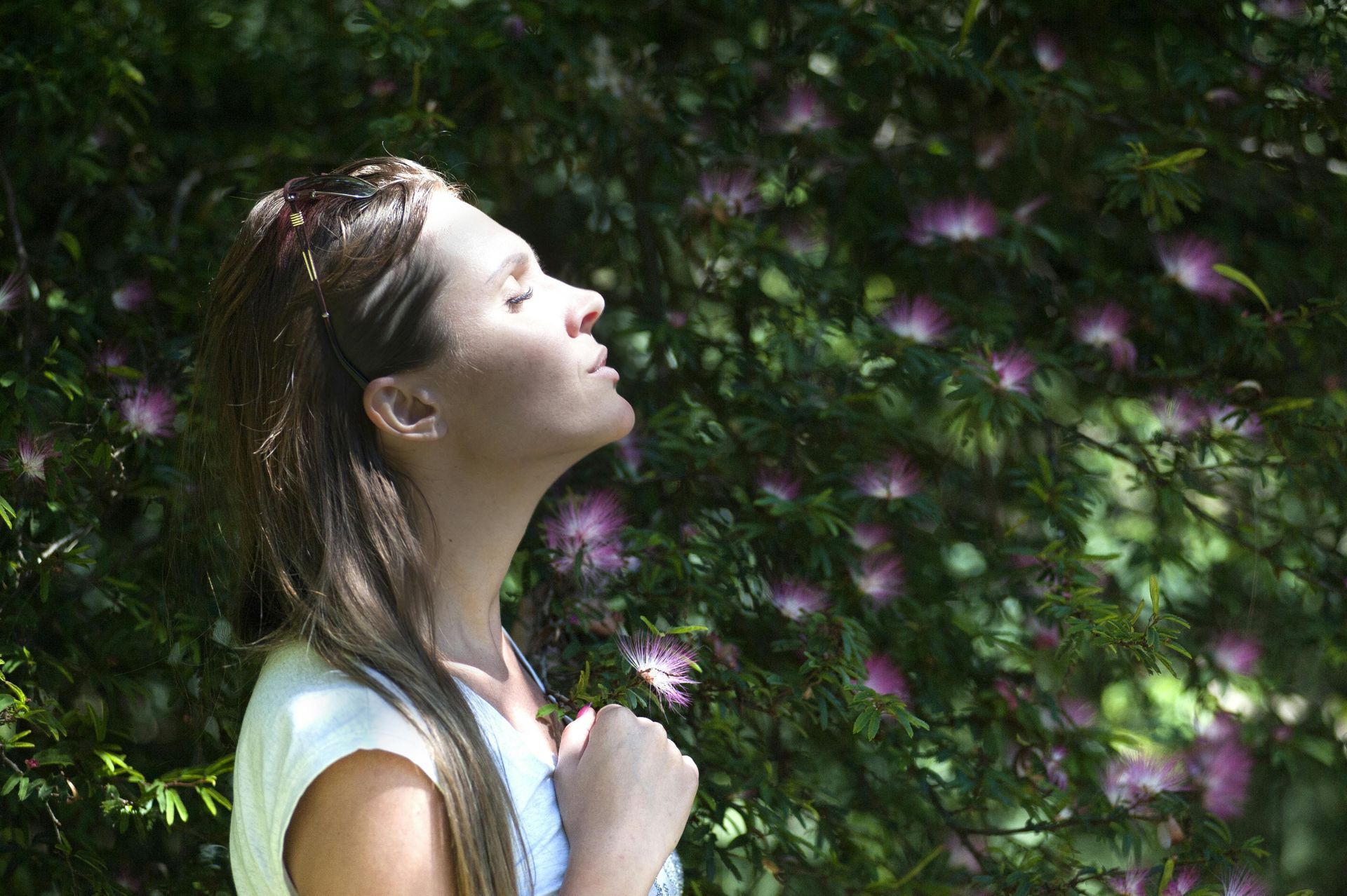 A woman is standing in front of a tree with her eyes closed.