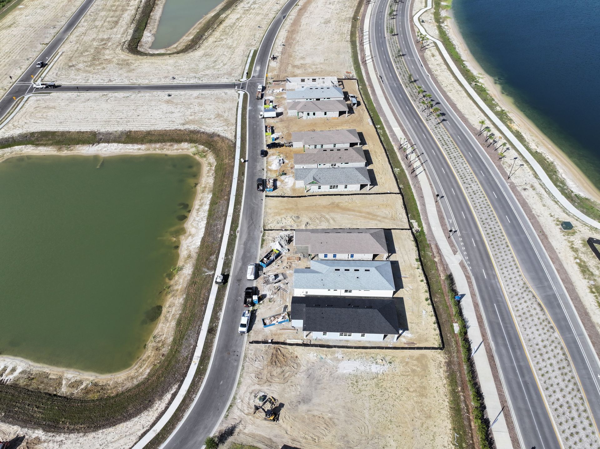 Aerial view of coastal road, water reservoir, and rows of houses beside a shoreline highway.