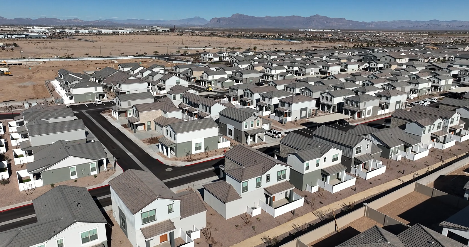 Aerial view of a suburban neighborhood with rows of houses and distant mountains under a clear sky