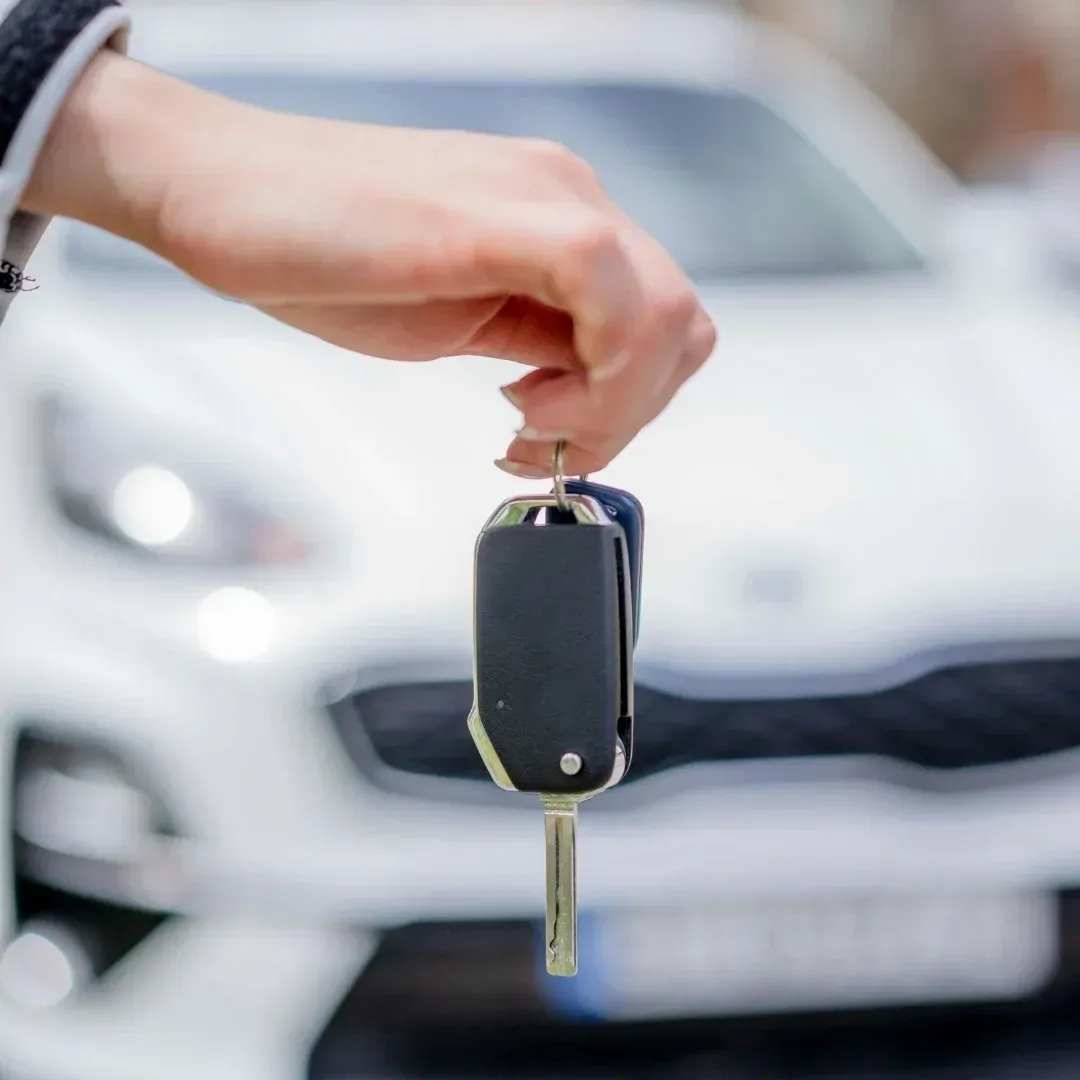 Hand holding a car key in front of a blurred white car Hand holding a car key in front of a blurred white car