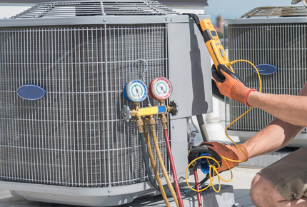 Technician using gauges to service an outdoor HVAC unit with a yellow tool and hoses attached