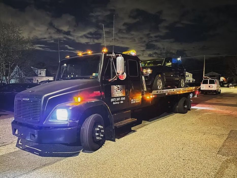A black tow truck is parked in a gravel lot at night.
