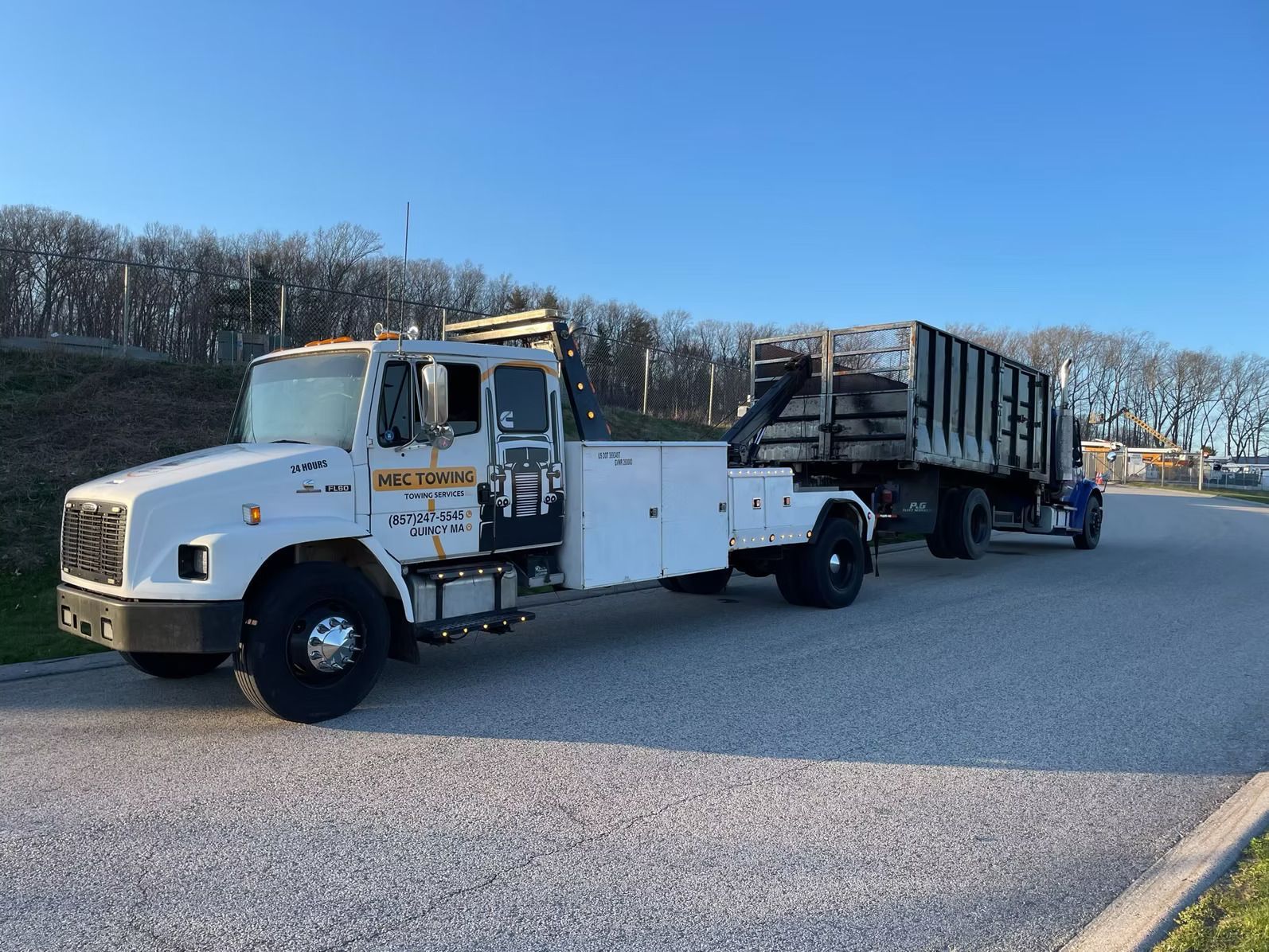 A white tow truck is parked on the side of the road next to a dump truck.