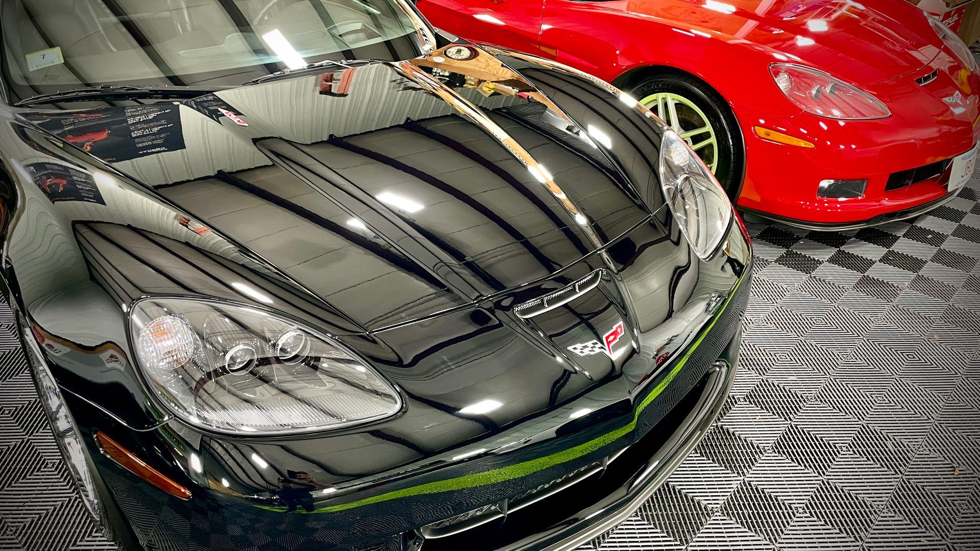 A black car is parked next to a red car in a garage.