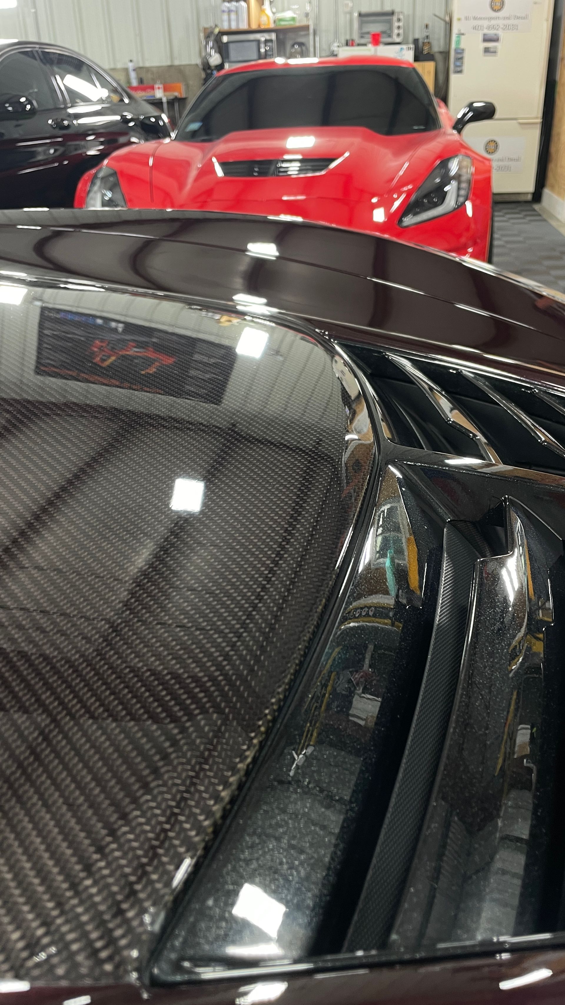 A black car is parked next to a red car in a garage.