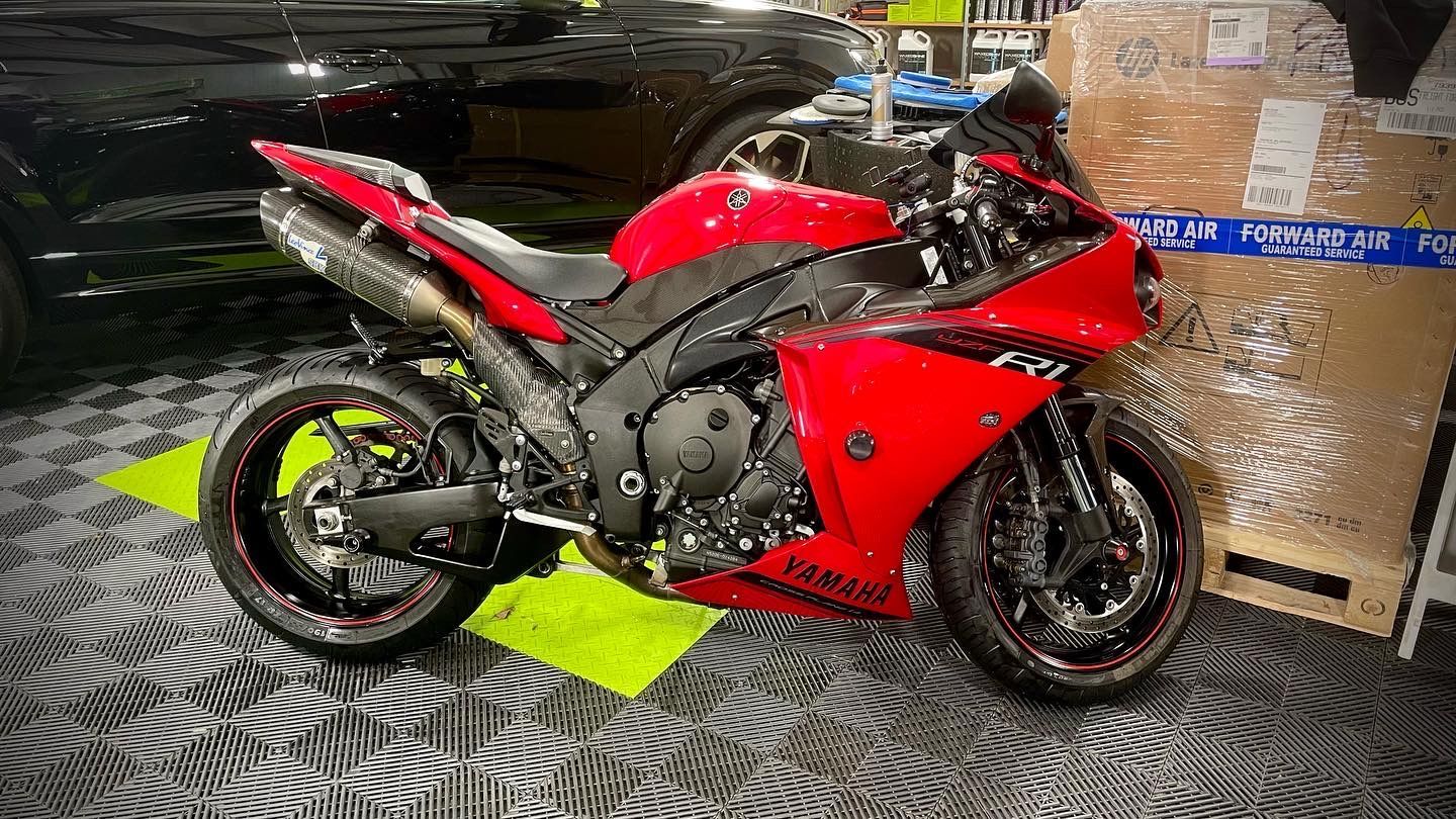 A red motorcycle is parked in a garage next to a black car.