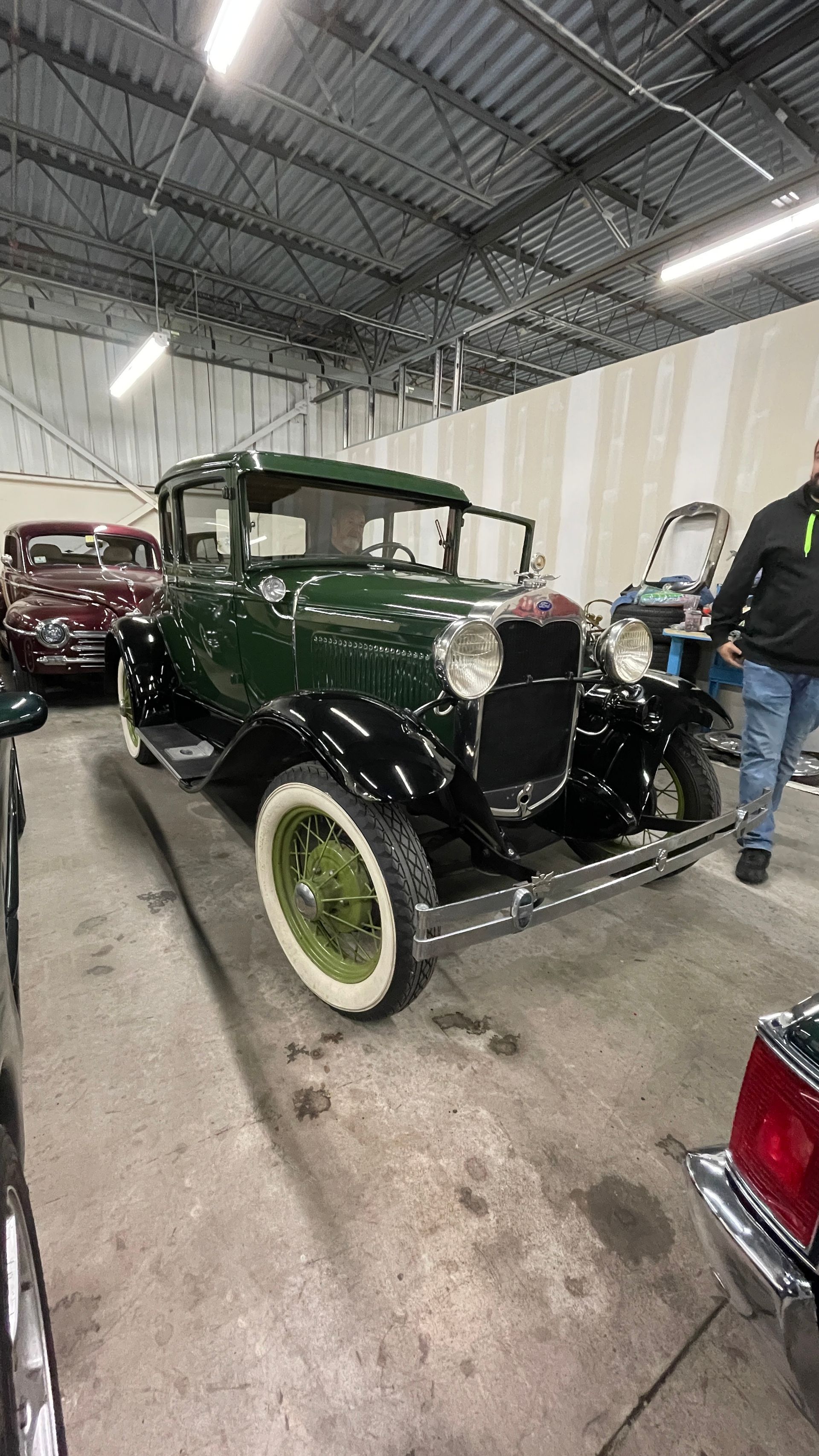 A man is standing next to a green car in a garage.