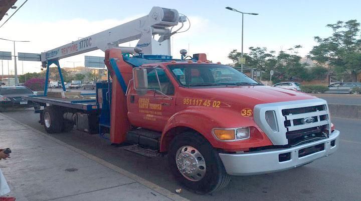 Una grúa roja con una grúa en la parte trasera está estacionada al costado de la carretera.