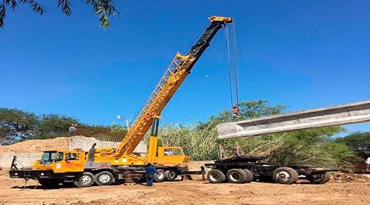 Una gran grúa amarilla está levantando una viga de hormigón en un remolque.