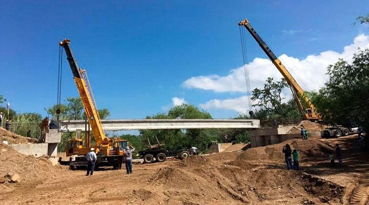 Dos grúas están levantando un puente sobre un río.