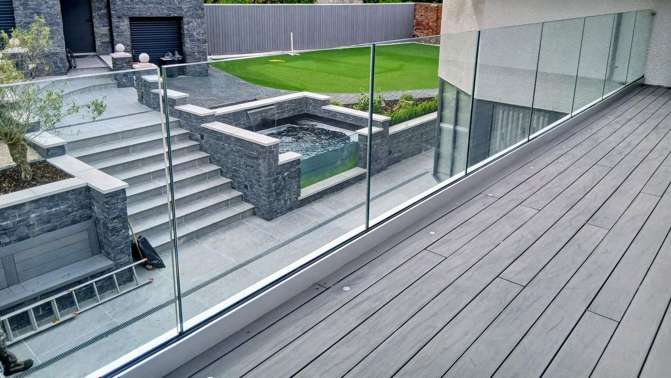 Modern deck with glass balustrade railing installed by Swansea Glass Balustrades. Hendrefoilan property overlooks a terraced backyard with steps, pool, and lawn.