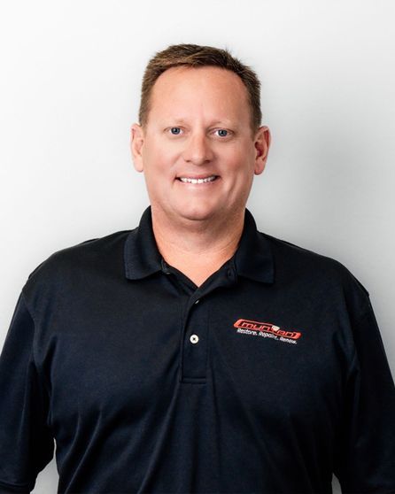 A man wearing a black shirt with a logo on it is smiling for the camera.