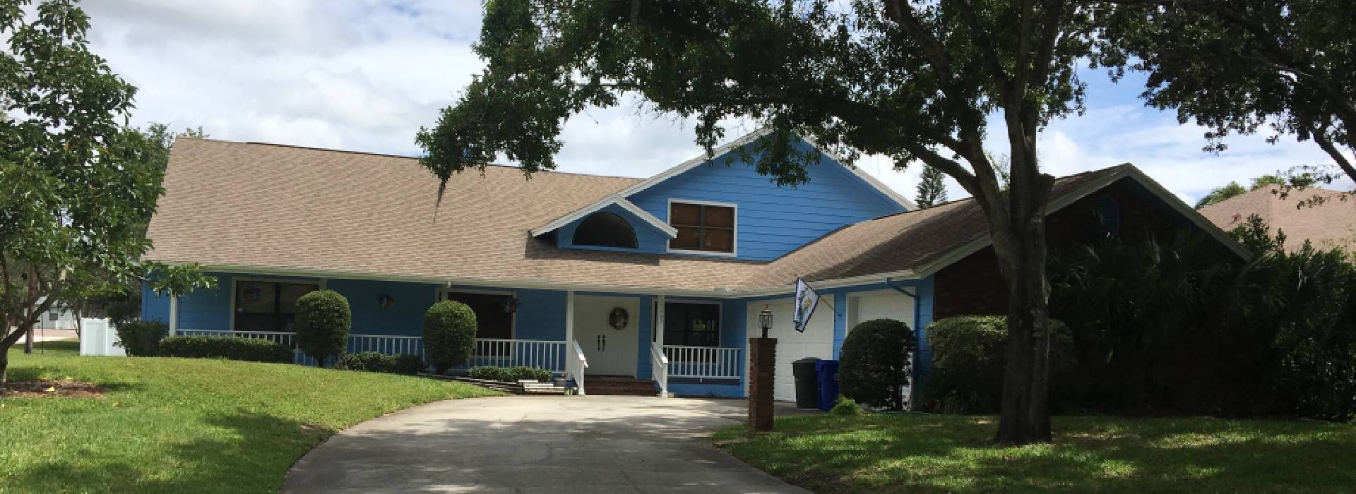 A blue house with a brown roof and a driveway leading to it