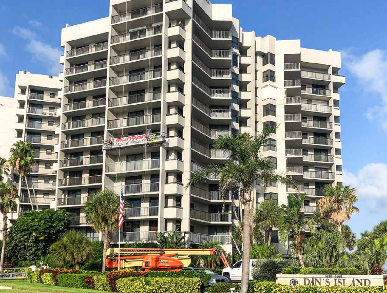 A large building with a lot of windows and balconies is surrounded by palm trees.