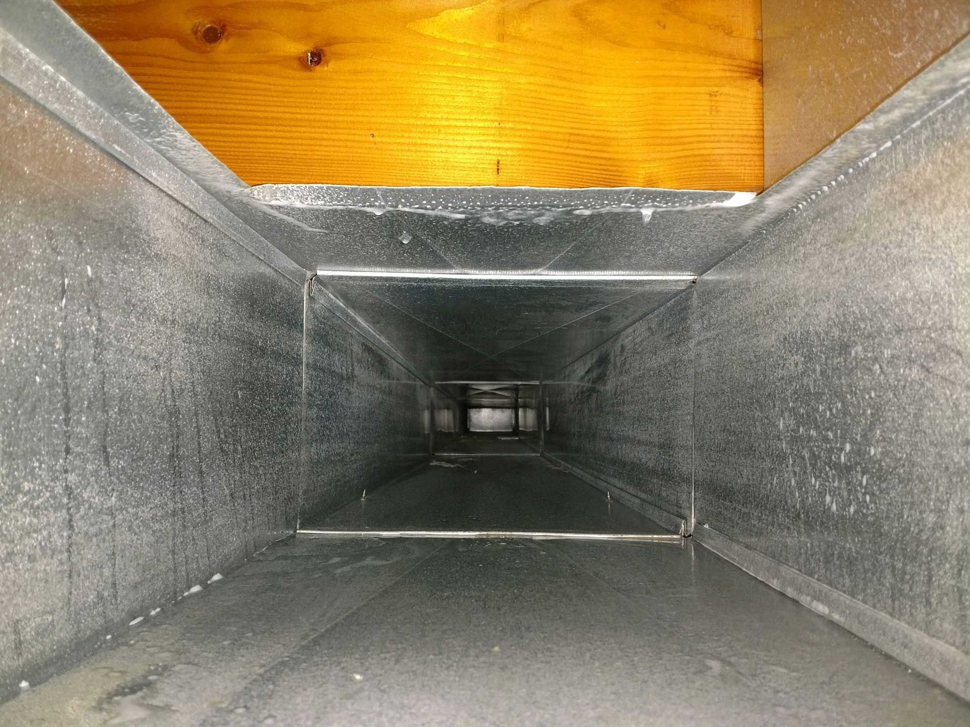 Inside of a rectangular metal air duct, with a wooden board above.