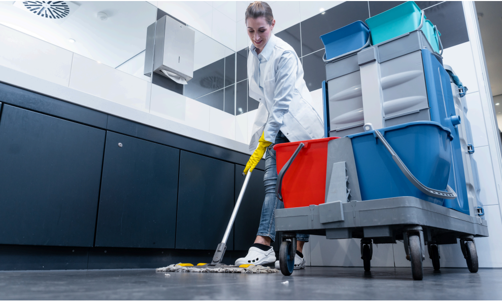 Cleaner moping floor next to cleaning cart.