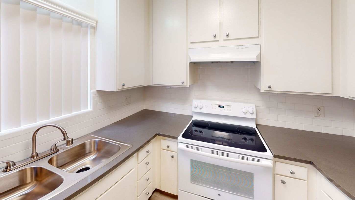 White kitchen with cabinets, stove, sink, and window with blinds.