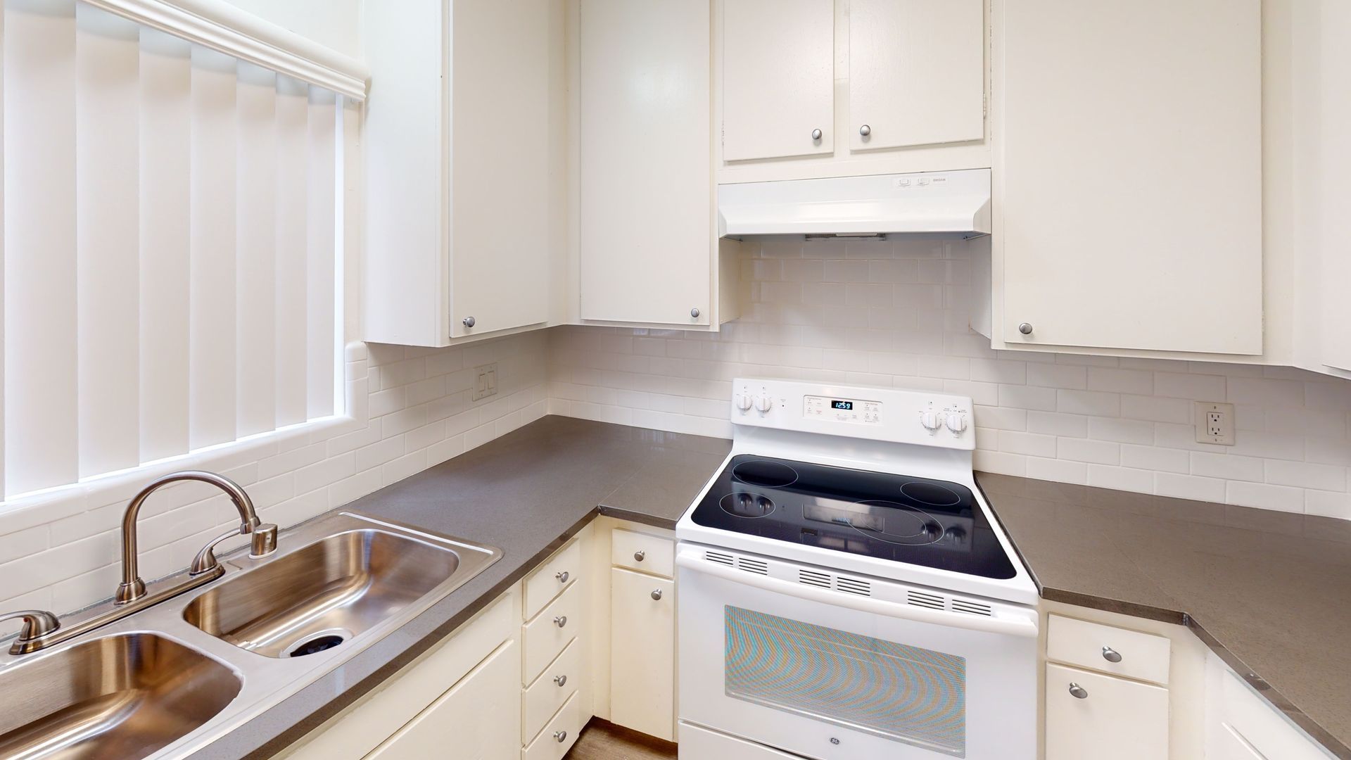 White kitchen with cabinets, stove, sink, and window with blinds.