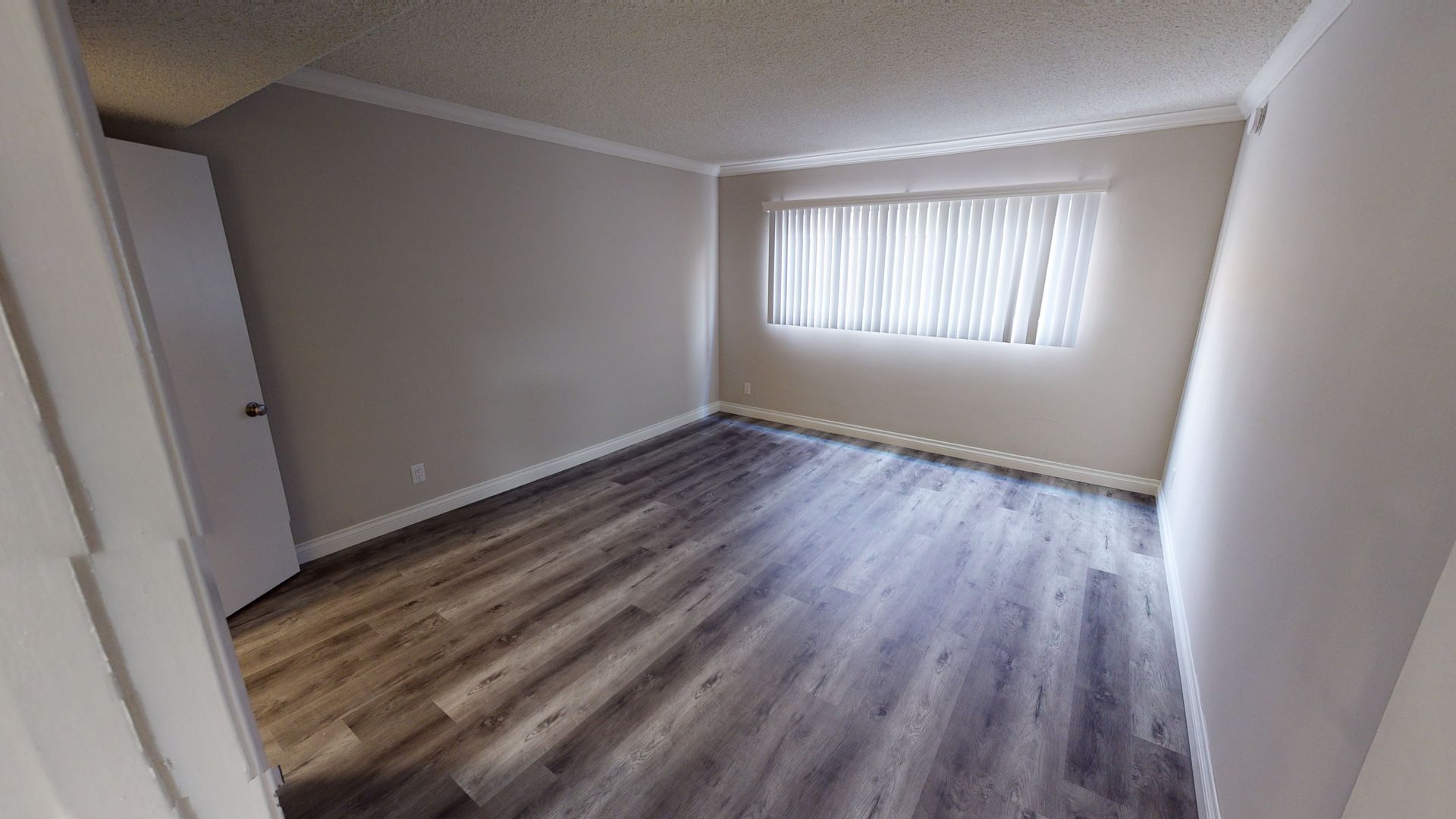 Empty bedroom with gray walls, wood-look flooring, and a window with curtains.
