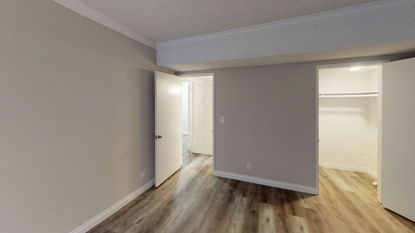 Empty bedroom with light wood-look flooring, three white doors, and neutral walls.