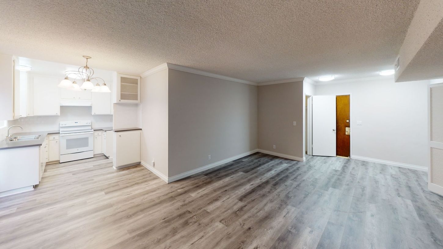 Interior of a modern apartment with light wood floors, white kitchen, and neutral walls.