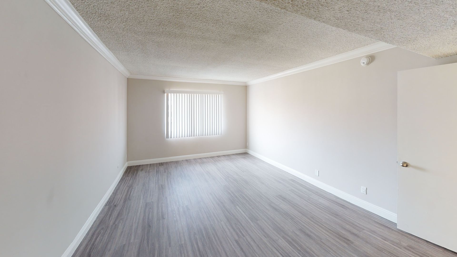 Empty room with wood-look flooring, window with blinds, and white walls and door.