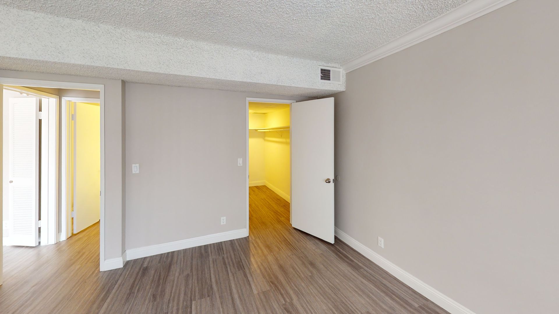 Empty bedroom with a closet and doors, painted gray walls and wood-look flooring.