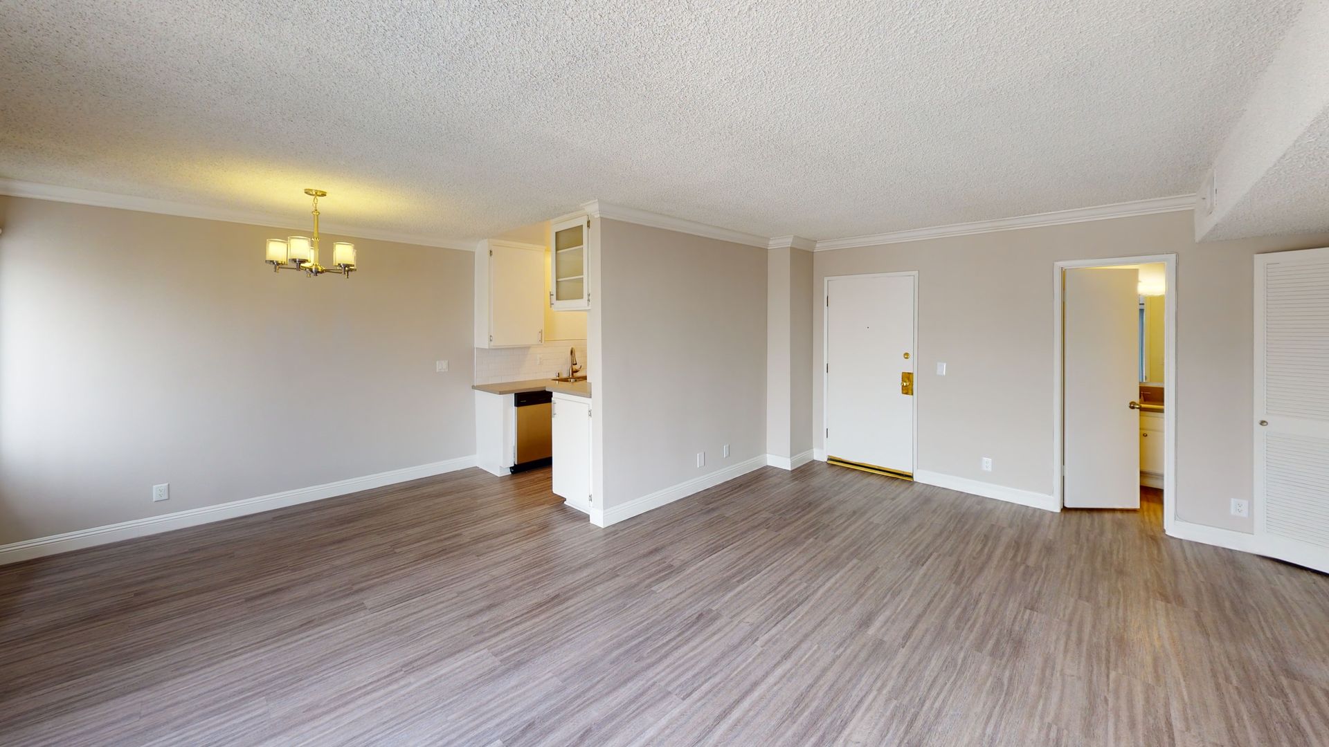 Empty apartment interior with wood-look flooring, light gray walls, and a small kitchen visible.