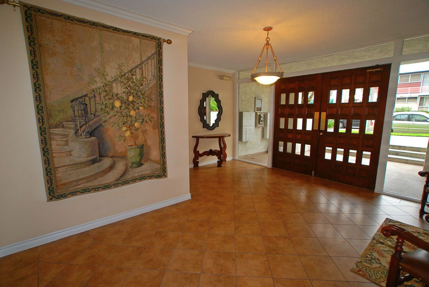 Entryway with large brown doors, tapestry, mirror, and tiled floor.