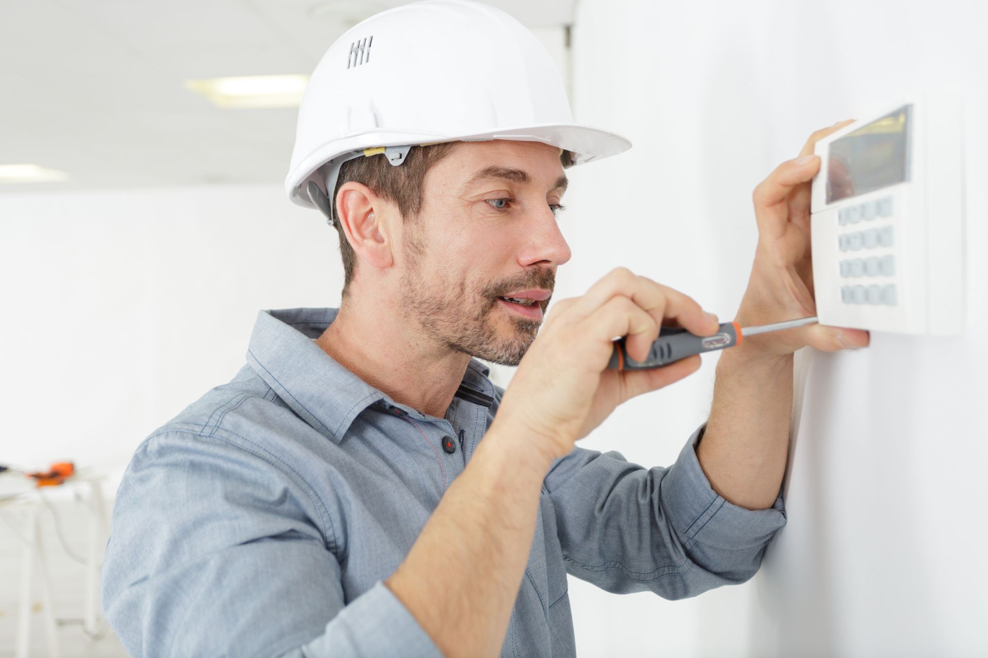 Man in hard hat using a screwdriver to install a white security keypad on a wall.