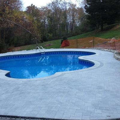 A large swimming pool is surrounded by a brick patio