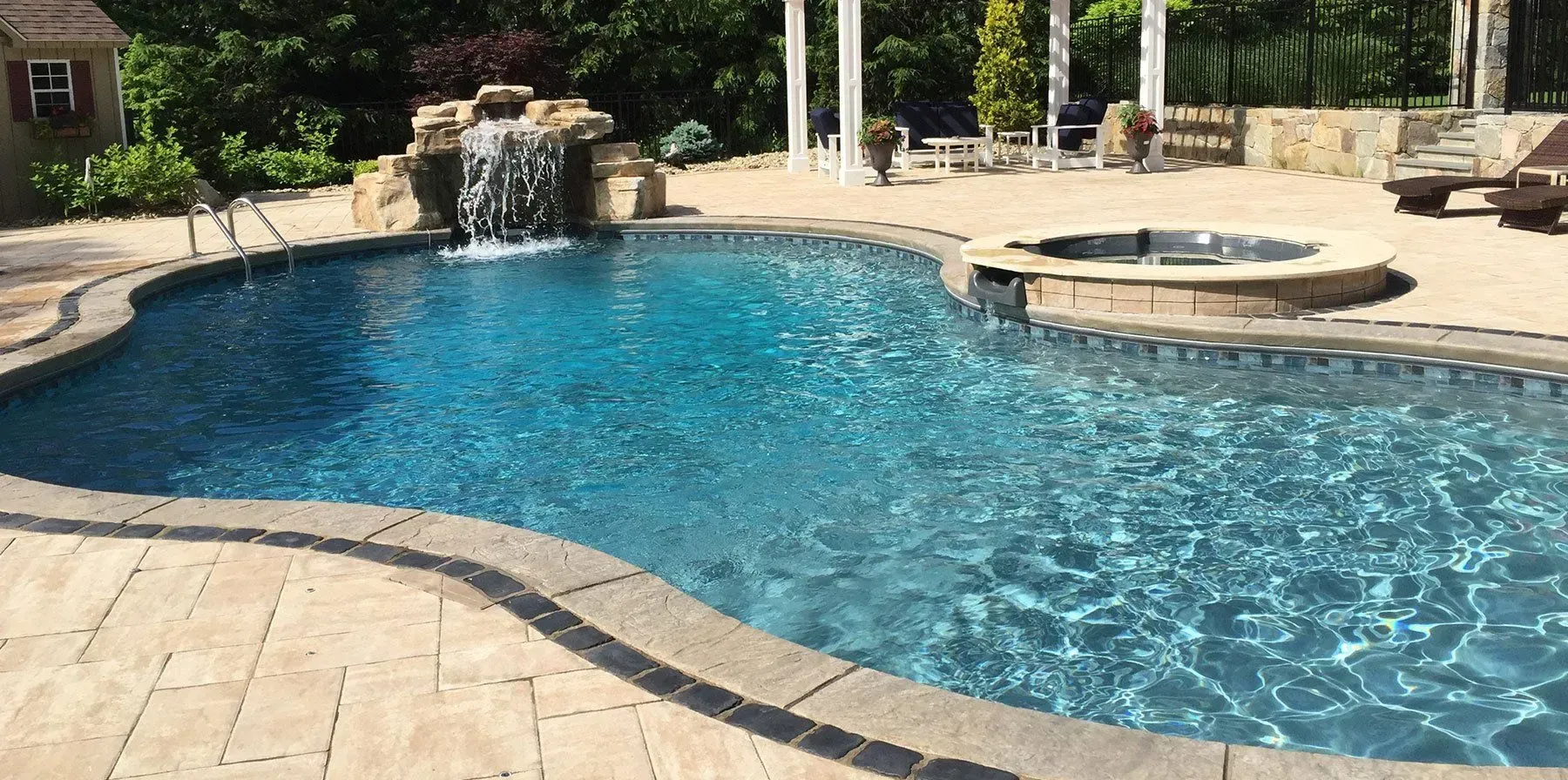 A large swimming pool with a waterfall in the backyard.